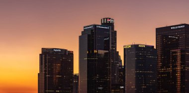 Los Angeles şehir merkezinin bir resmi, gökdelenleri logolarla kaplı, günbatımında.