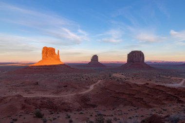 Batı Mitten Butte, Doğu Mitten Butte ve Merrick Butte kaya oluşumlarıyla gün batımında Anıt Vadisi manzarasının bir resmi..