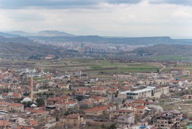 Arka planda Nevsehir şehrinin resmi, ve önplanda Uchisar kasabasının, bulutlu bir günde.