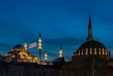 Rustem Paşa Camii 'nin kubbesi ve Süleyman Camii' nin gece yarısı çekilmiş bir resmi. Tabelada 