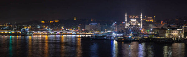A panorama picture of the Galata Bridge and the New Mosque at night. The sign on the mosque reads as "Find life with Quran".