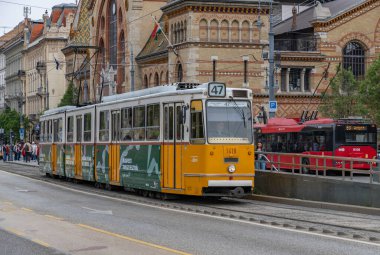 Merkez Pazar Salonunun yanında sarı bir Budapeşte tramvayı resmi..