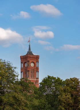 Rotes Rathaus 'un ya da Berlin Red City Hall' un ağaç tepelerinin üstündeki kulesinin bir resmi..