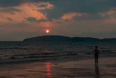 Ao Nang Sahili 'nde gün batımını izleyen bir kadının resmi..