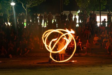 Gece Ao Nang Sahili 'ndeki yangın gösterisinin resmi. Burada, sanatçı tekerlekli sandalyede ve kalabalıktan bir kadının etrafında ateşle oynuyor..