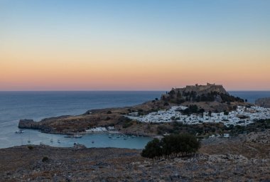 Lindos kasabasının ve gün batımında çevreleyen manzaranın resmi..