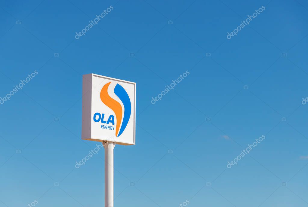 A picture of the OLA Energy sign next to a gas station against a blue sky.