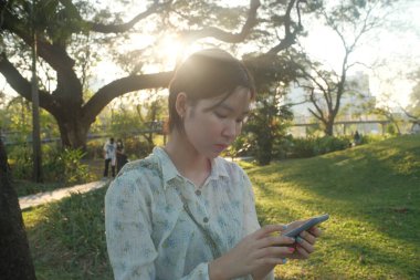 Genç bir kadın güneş ışığı parkı akıllı telefonu dışarıda sakin bir ortam tabiat ilkbaharı