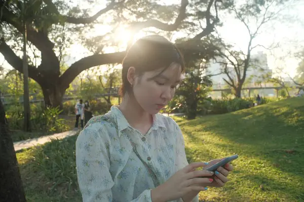Genç bir kadın güneş ışığı parkı akıllı telefonu dışarıda sakin bir ortam tabiat ilkbaharı