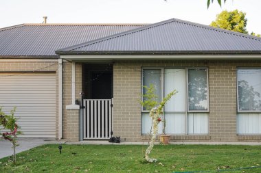 Önünde yeşil çimenler ve küçük ağaçlar olan modern bir tuğla ev.