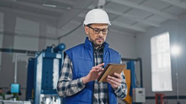 Gözlüklü beyaz adam daha iyi görebilmek için mesaj yazıyor ya da tablet cihazına bilgi giriyor. Akıllı yönetici üretim çizgileri arasında yürüyor. Üretim kapasitesi hesaplanıyor.