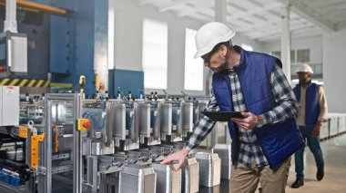 Tablet bilgilerini kontrol eden orta yaşlı beyaz fabrika çalışanının yakın plan portresi. Kaskın üretim sürecini analiz eden kasten üretilmiş bir uzman..