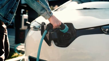 Erkek eli şarj kablosu tutarken ve EV şarj istasyonunun dışındaki elektrikli bir arabanın fişini çekerken. İnsan eli elektrikli aracı şarj etmeye başlar. Şehir hayatı, şehir tarzı. Eko araba. Şarj noktası
