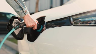 Dışarıdaki elektrikli arabasını şarj etmek için kablo kullanan adamı yakından çek. Erkek olan şarj kablosunu caddedeki şarj limanına bağlıyor. EV teknoloji konsepti. Gelecekteki otomobil şarj istasyonu