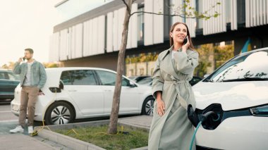 Gençler şehirdeki şarj istasyonunda elektrikli arabalara teleferik koyuyorlar. Güzel, neşeli bir kadın elektrikli aracını şarj ederken dışarıdaki akıllı telefondan arıyor. Şarj noktası. Sıfır emisyon. Eko araba