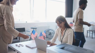 Amerika Birleşik Devletleri Seçimlerinde oy kullanmak için sandığa gelen Afrikalı Amerikalı bir adamın kamera görüntüsü. Oy pusulası almak için kayıt yaptıran adam. Seçmen belgelerini dizüstü bilgisayarda kontrol eden tatlı kız..