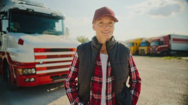 Kamera, kırmızı beysbol şapkalı güzel beyaz kadına yaklaşıyor. Kareli gömlek ve siyah yelek giyiyor. Gülümserken kameraya bakmak. Arka planda muhteşem bir kargo aracı var..