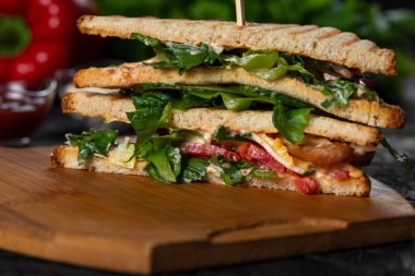 Domuz pastırmalı ve ahşap tahtada yeşillikli sandviçlerin yakın plan çekimi.