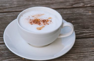 Ahşap masa arkasında köpüklü bir fincan kahve.