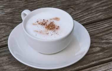 Ahşap masa arkasında köpüklü bir fincan kahve.