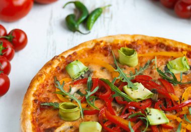 Peynirli, domatesli, biberli ve ahşap masadaki avokadolu vejetaryen pizzası.