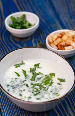 Yoğurt çorbası, mavi ahşap bir masada otlar ve krakerler.