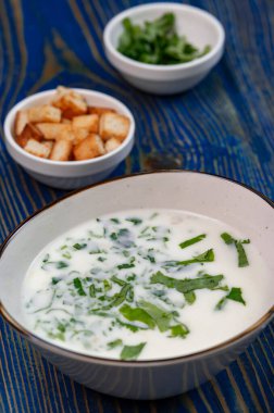 Yoğurt çorbası, mavi ahşap bir masada otlar ve krakerler.