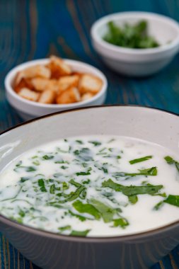 Yoğurt çorbası, mavi ahşap bir masada otlar ve krakerler.