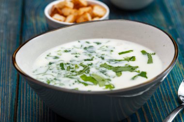 Yoğurt çorbası, mavi ahşap bir masada otlar ve krakerler.