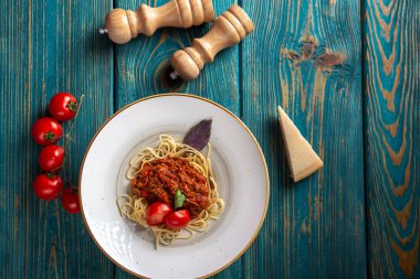 Etli makarna, domates sosu ve mavi ahşap masada sebzeler. en üstteki görünüm