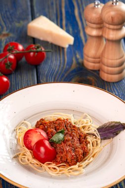Beyaz tabakta spagetti bolonez makarna, tuz, biber, peynir ve domates mavi ahşap arka planda..