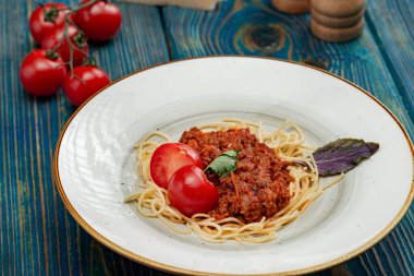 Etli makarna, domates sosu ve mavi ahşap masada sebzeler.