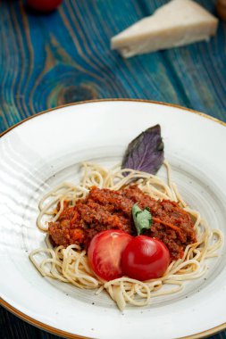 Etli makarna, domates sosu ve mavi ahşap masada sebzeler.