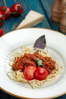 Etli makarna, domates sosu ve mavi ahşap masada sebzeler.