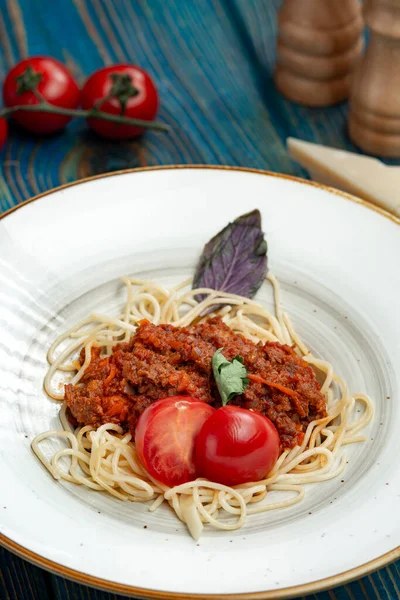 Pasta with meat, tomato sauce and vegetables in blue wooden desk