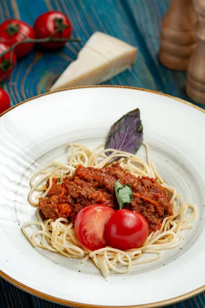 Pasta with meat, tomato sauce and vegetables in blue wooden desk
