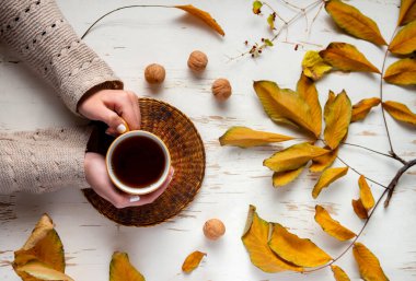 Süveter tutan kadın elleri çay fincanı ve eski ahşap masa üzerinde kurumuş yaprak açık kitap. Sonbahar konsepti. Yaklaş, seçici odaklanma