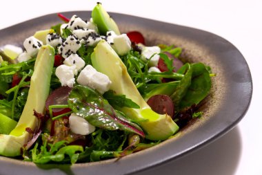 Bowl of vegetables salad with avocado on white background