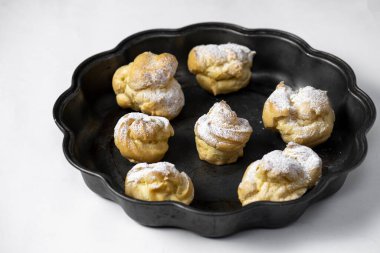 Decorating profiteroles with powdered sugar on black plate