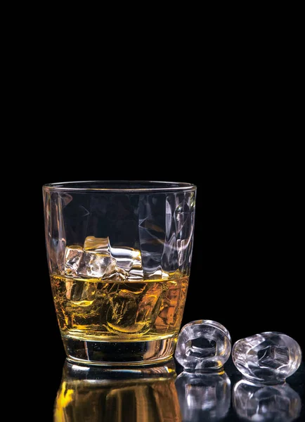 Whisky glass with ice cubes on black background