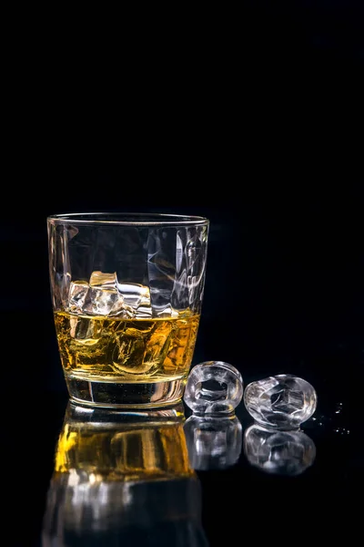 Whisky glass with ice cubes on black background