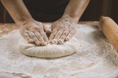 Kadın elleri ahşap bir masada hamur yoğuruyor.