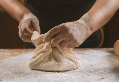 Kadın elleri ahşap bir masada hamur yoğuruyor.