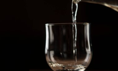 Siyah arka plandaki kil şişeden bardağa şarap dökülüyor.