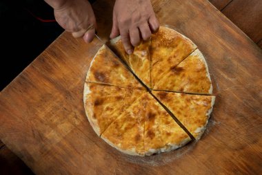 Ahşap arka planda ev yapımı etli turta kesen kişi. Bulgar banitsa, Gürcü khachapuri, Yunan tiropita