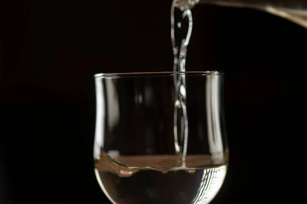 stock image pouring wine into glass from clay bottle on black background