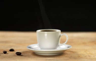 Kahve fincanı ve kahve çekirdekleri ahşap masada. Siyah arkaplan.