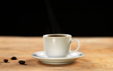 Kahve fincanı ve kahve çekirdekleri ahşap masada. Siyah arkaplan.