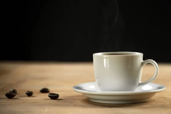 stock image Coffee cup and coffee beans on wooden table. Black background.