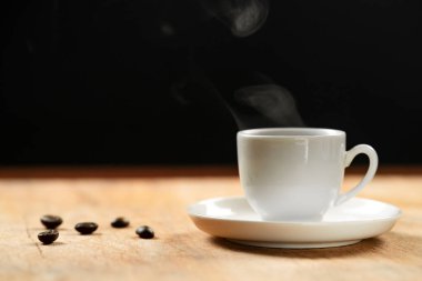 Kahve fincanı ve kahve çekirdekleri ahşap masada. Siyah arkaplan.